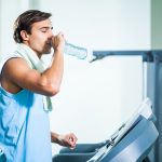 Man drinking water while exercising in gym